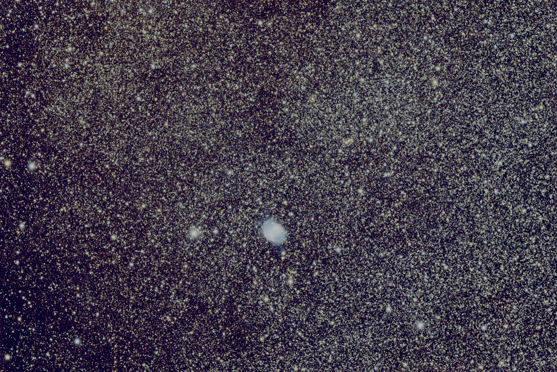 The Dumbbell Nebula, a small pale shell in a wide star field.